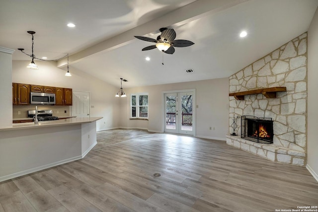 unfurnished living room featuring vaulted ceiling with beams, ceiling fan, light hardwood / wood-style floors, and a stone fireplace