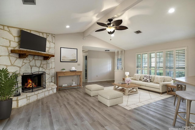 living room featuring vaulted ceiling with beams, light hardwood / wood-style floors, a stone fireplace, and ceiling fan