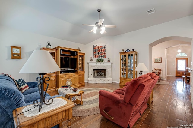 living room with lofted ceiling, a stone fireplace, dark hardwood / wood-style floors, and ceiling fan