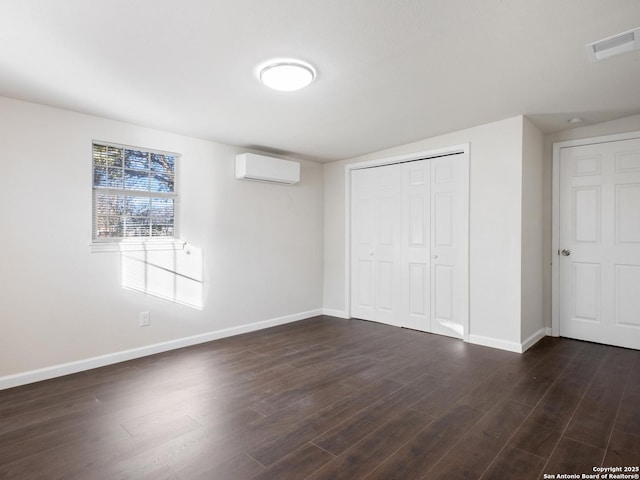 unfurnished bedroom with a wall unit AC, a closet, and dark wood-type flooring