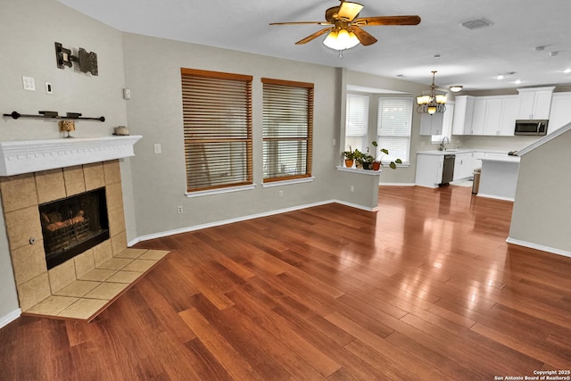 unfurnished living room with ceiling fan with notable chandelier, hardwood / wood-style floors, sink, and a tiled fireplace