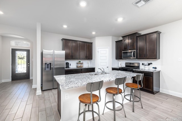 kitchen with light stone countertops, sink, decorative backsplash, a center island with sink, and appliances with stainless steel finishes