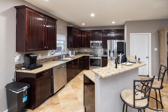 kitchen featuring a center island, a kitchen breakfast bar, sink, appliances with stainless steel finishes, and light stone counters