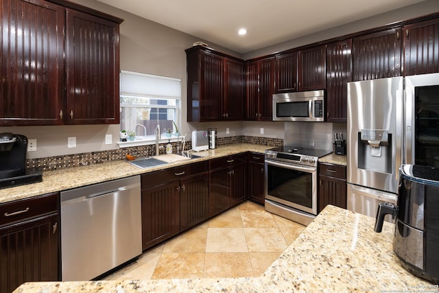 kitchen with dark brown cabinets, stainless steel appliances, light stone counters, and sink