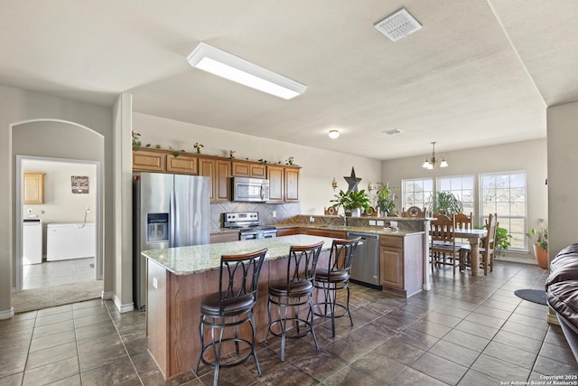 kitchen with kitchen peninsula, appliances with stainless steel finishes, pendant lighting, a chandelier, and a center island