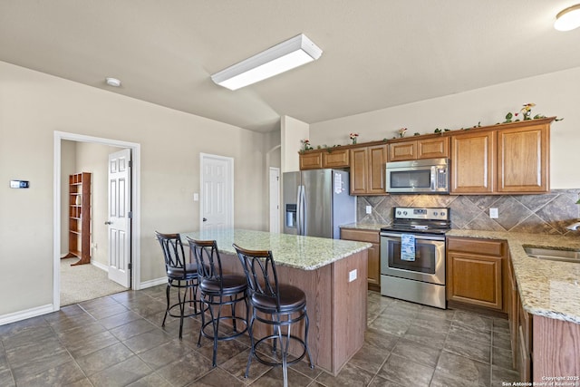 kitchen with a center island, decorative backsplash, appliances with stainless steel finishes, light stone counters, and a breakfast bar area