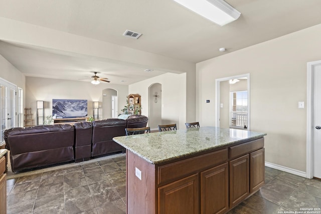 kitchen with ceiling fan, a center island, and light stone counters