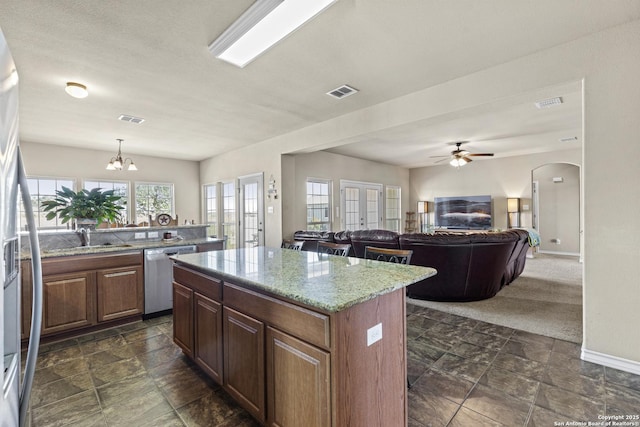 kitchen with a kitchen island, light stone countertops, hanging light fixtures, and stainless steel appliances