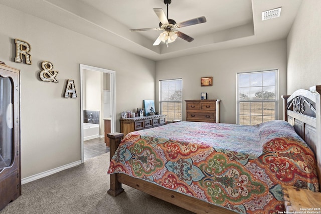 carpeted bedroom featuring ceiling fan, a tray ceiling, and ensuite bath