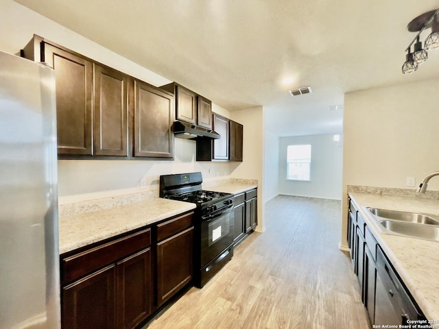 kitchen featuring light stone countertops, light wood-type flooring, dark brown cabinetry, stainless steel appliances, and sink