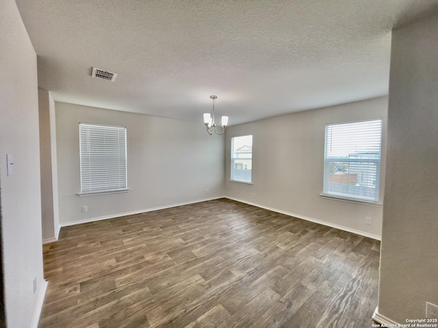 unfurnished room with a textured ceiling, an inviting chandelier, and dark wood-type flooring