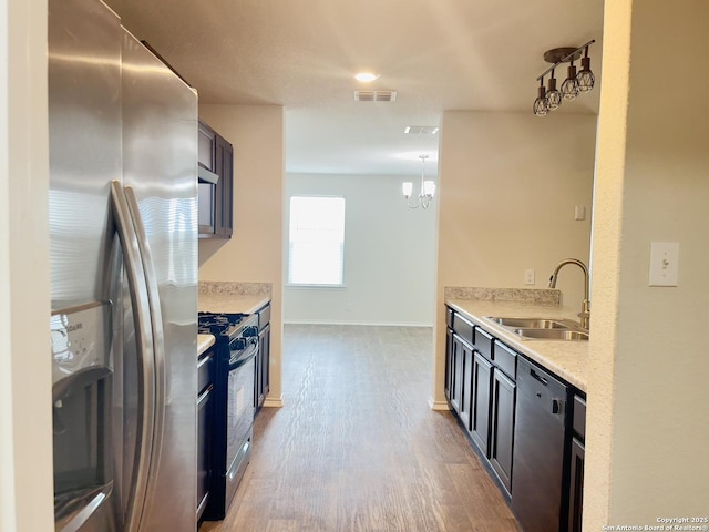 kitchen with light stone countertops, sink, stainless steel appliances, a notable chandelier, and light hardwood / wood-style floors