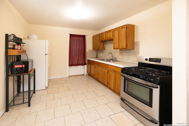 kitchen featuring backsplash, white refrigerator, sink, stainless steel gas stove, and light tile patterned floors