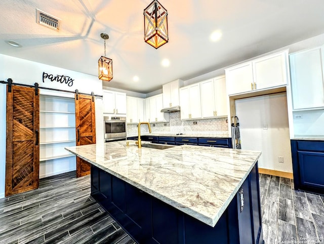 kitchen featuring white cabinets, decorative light fixtures, a barn door, and stainless steel oven