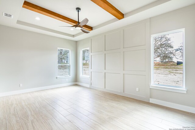 empty room featuring beamed ceiling, light wood-type flooring, a tray ceiling, and ceiling fan