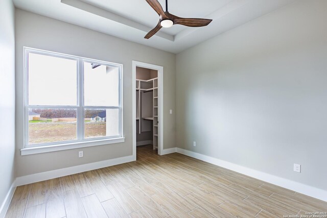 unfurnished bedroom with light wood-type flooring, a walk in closet, a closet, and ceiling fan