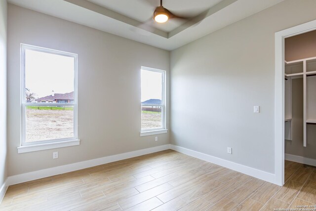 unfurnished bedroom with a raised ceiling, a walk in closet, a closet, and light hardwood / wood-style flooring