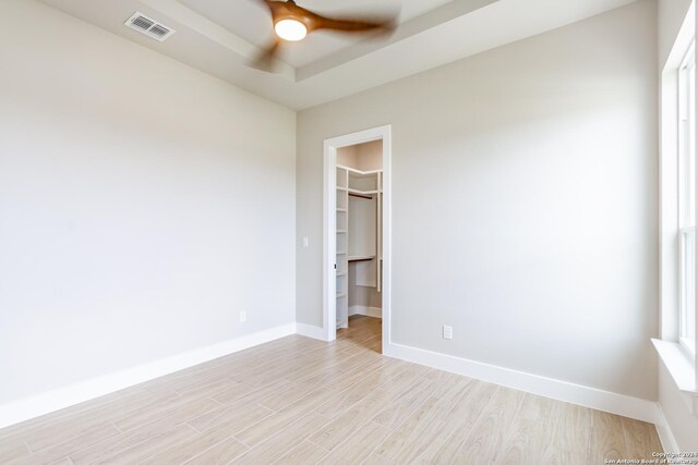 empty room with a raised ceiling, ceiling fan, and light hardwood / wood-style floors