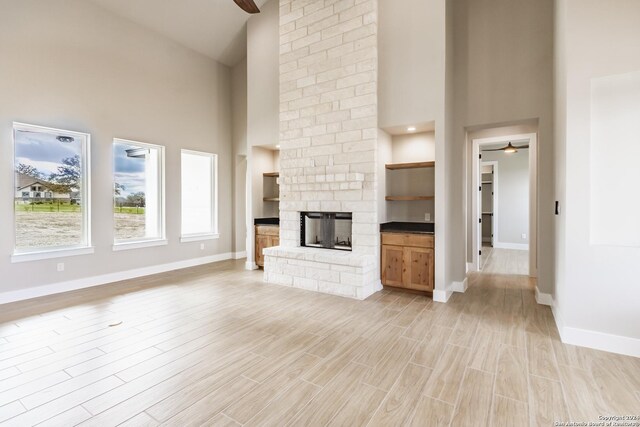 unfurnished living room with a stone fireplace, ceiling fan, light hardwood / wood-style flooring, and a high ceiling