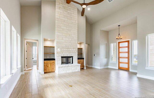 unfurnished living room featuring beam ceiling, a fireplace, high vaulted ceiling, and ceiling fan with notable chandelier