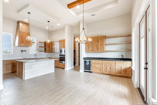 kitchen with a center island with sink, sink, hanging light fixtures, stainless steel appliances, and beverage cooler