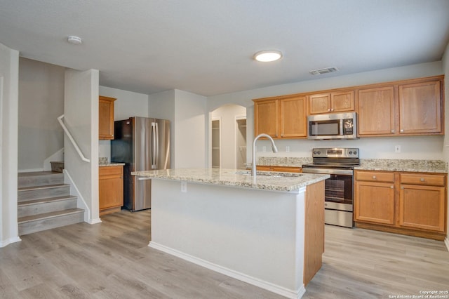 kitchen with appliances with stainless steel finishes, sink, light hardwood / wood-style flooring, and an island with sink