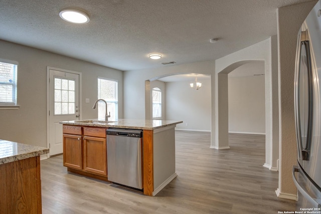 kitchen featuring sink, light stone countertops, stainless steel appliances, and an island with sink