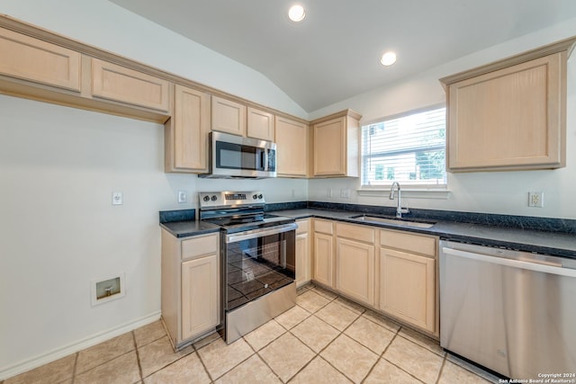 kitchen with light brown cabinets, sink, lofted ceiling, light tile patterned floors, and appliances with stainless steel finishes