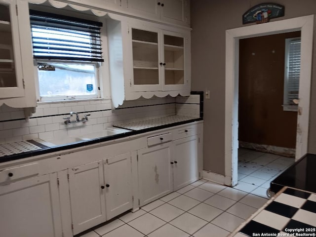 kitchen with tasteful backsplash, sink, white cabinets, and light tile patterned floors