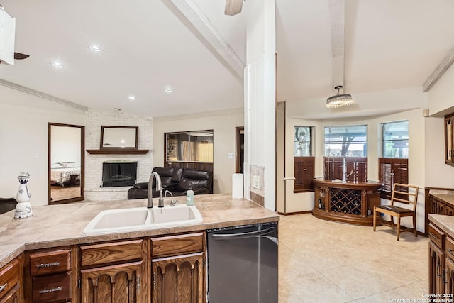 kitchen featuring sink, decorative light fixtures, dishwasher, beamed ceiling, and a brick fireplace