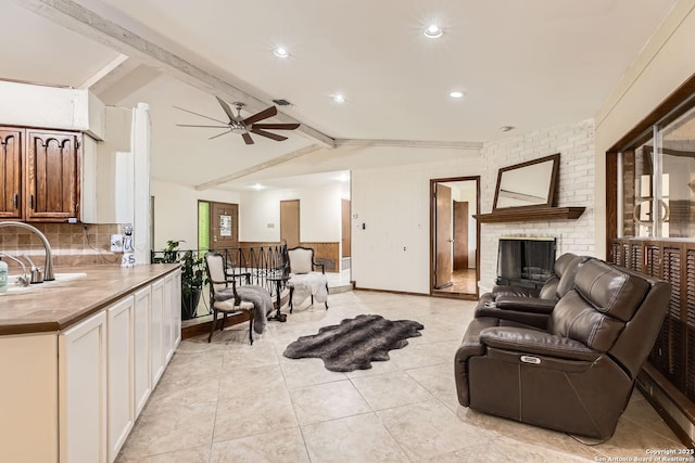 living room featuring lofted ceiling with beams, ceiling fan, a fireplace, light tile patterned flooring, and sink