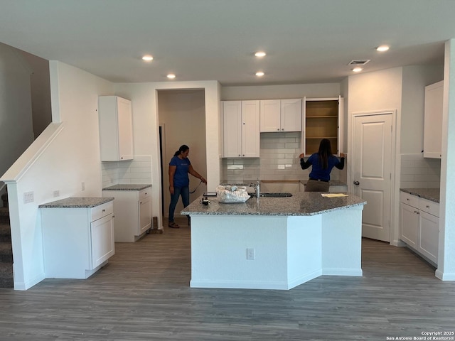 kitchen featuring dark hardwood / wood-style flooring, backsplash, white cabinetry, and an island with sink