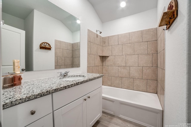 bathroom featuring vanity, wood-type flooring, tiled shower / bath combo, and lofted ceiling