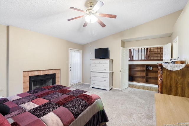 bedroom with lofted ceiling, light colored carpet, a textured ceiling, ceiling fan, and a tiled fireplace