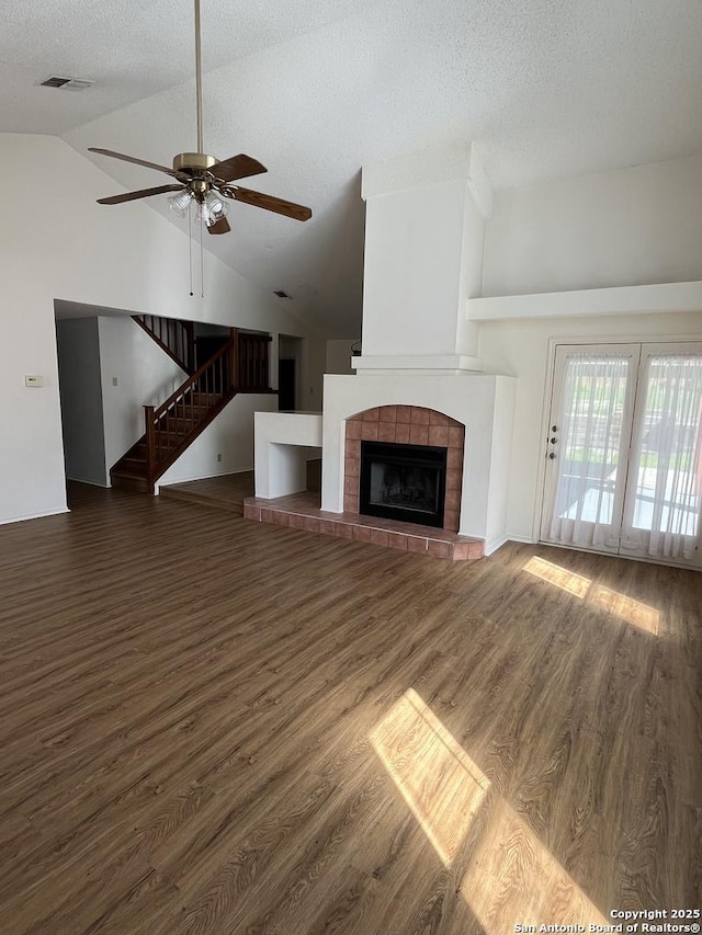 unfurnished living room with lofted ceiling, dark wood-type flooring, a tile fireplace, ceiling fan, and a textured ceiling