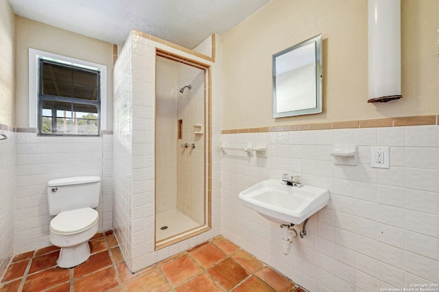 bathroom featuring a tile shower, sink, a textured ceiling, toilet, and tile walls