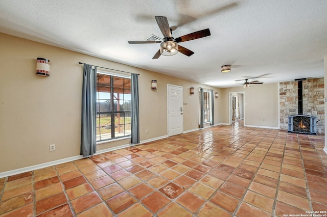 unfurnished living room with ceiling fan, a wood stove, a textured ceiling, and light tile patterned floors