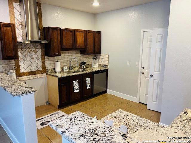 kitchen featuring decorative backsplash, light stone counters, wall chimney exhaust hood, sink, and light tile patterned floors