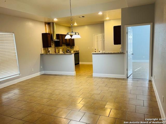 kitchen with kitchen peninsula, tasteful backsplash, dark brown cabinetry, wall chimney range hood, and hanging light fixtures