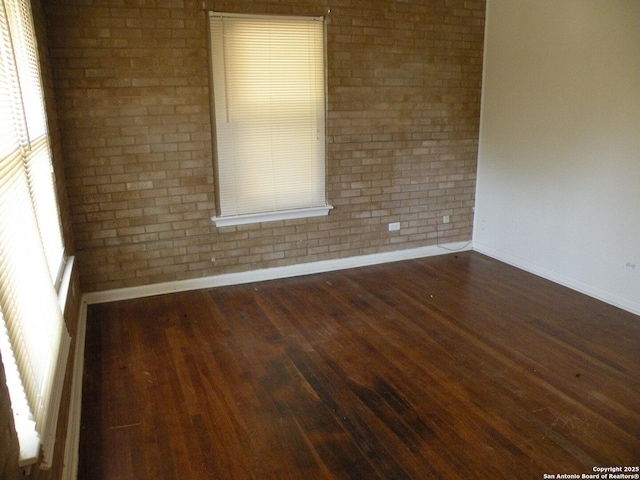 empty room with dark hardwood / wood-style flooring and brick wall