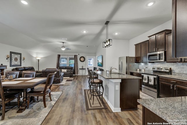 kitchen featuring a center island with sink, sink, vaulted ceiling, light stone counters, and stainless steel appliances