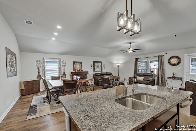 kitchen featuring sink, light stone counters, decorative light fixtures, a center island with sink, and ceiling fan with notable chandelier