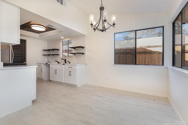 unfurnished dining area featuring sink, a tray ceiling, and a chandelier