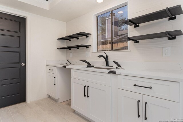 bar with light stone countertops, white cabinetry, and sink