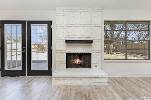 unfurnished living room featuring plenty of natural light, wood-type flooring, a fireplace, and french doors