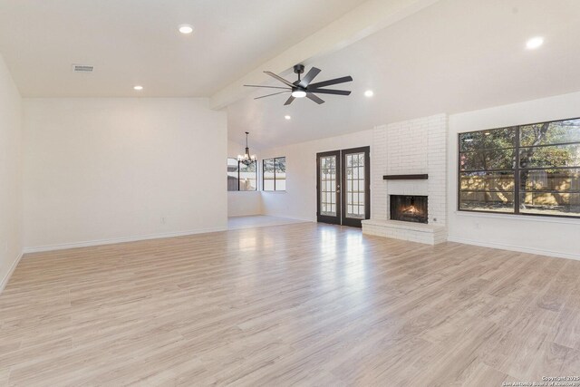 unfurnished living room with lofted ceiling with beams, light wood-type flooring, ceiling fan with notable chandelier, and a brick fireplace