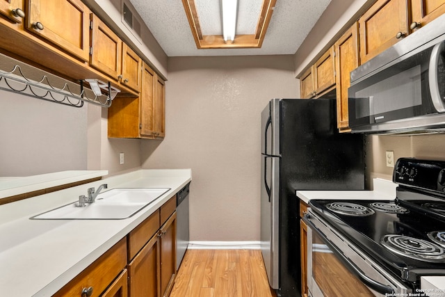 kitchen with sink, light wood-type flooring, a textured ceiling, and appliances with stainless steel finishes