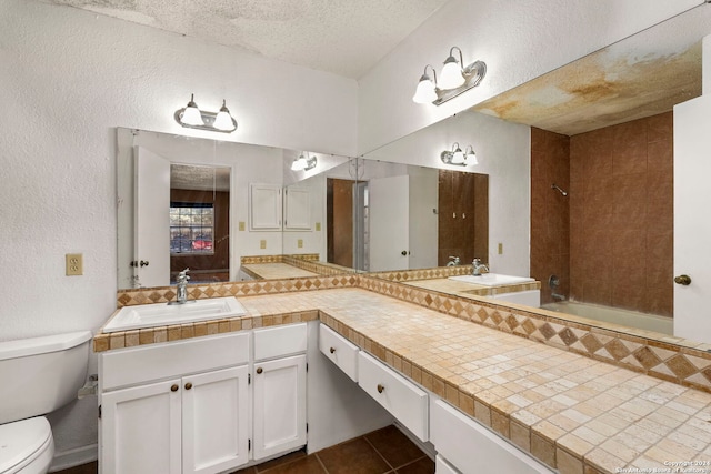 full bathroom featuring vanity, tile patterned floors, tiled shower / bath, toilet, and a textured ceiling