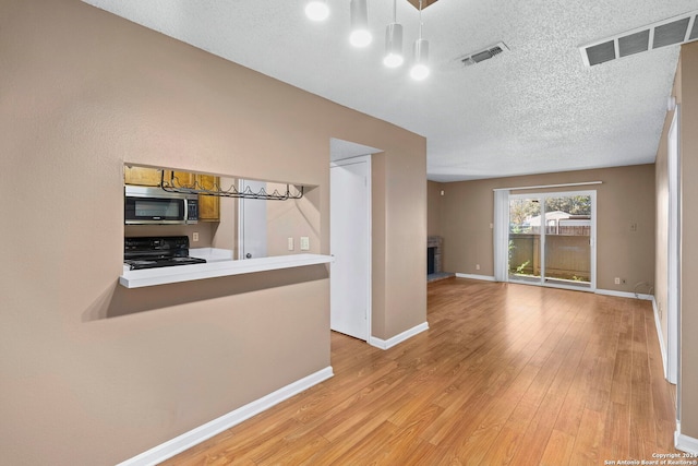 interior space featuring kitchen peninsula, black stove, a textured ceiling, and light hardwood / wood-style flooring