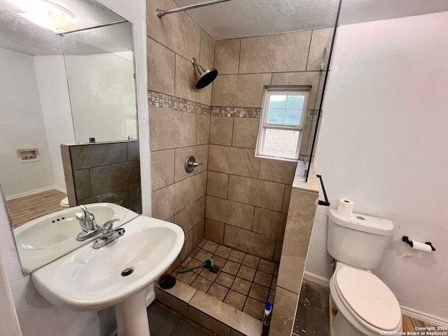 bathroom featuring sink, toilet, a textured ceiling, and tiled shower